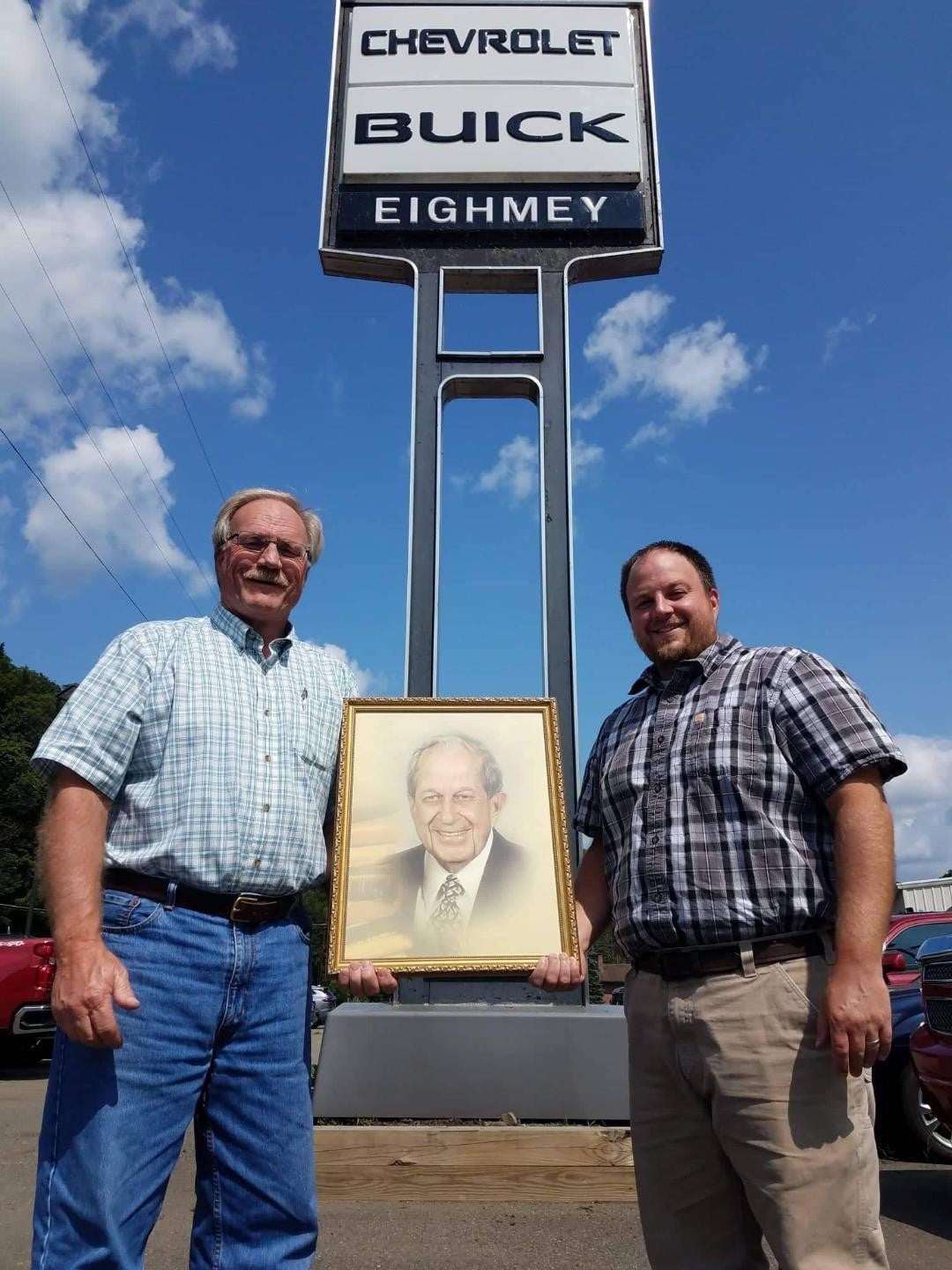 Two gentlemen holding a framed picture outside of Eighmey Chevrolet dealership